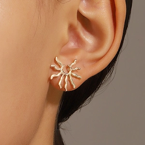 Gros plan d'une boucle d'oreille soleil doré avec rayons ondulés sur une oreille