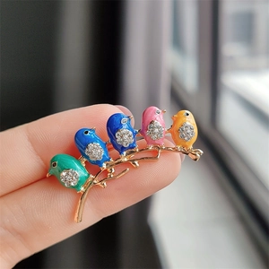 Detail of colorful enamel birds brooch with rhinestones on a gold branch held on fingertip