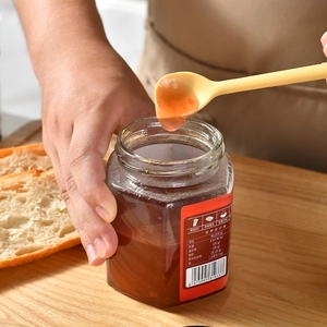 Double-ended silicone jam spatula scooping fruit spread from a glass jar on wood