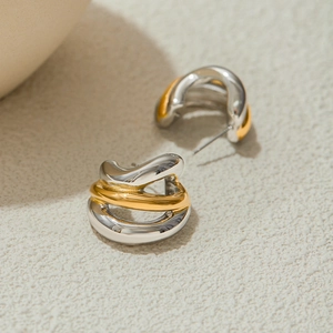 Macro detail of intertwined gold and silver stainless steel C-shaped earrings