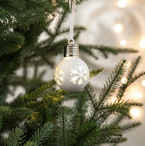 Glow-in-the-dark Christmas bulb ornament with snowflake pattern hanging on a tree branch