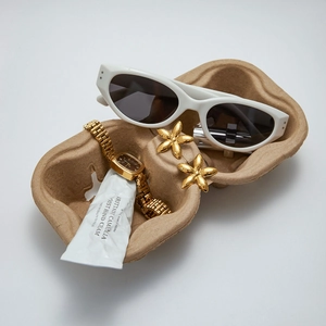 Flat lay of gold flower earrings with white sunglasses and a vintage watch on a tray