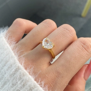 Detail of heart-cut clear zircon ring on finger with elegant golden band finish