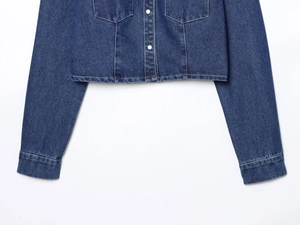 Detail view of the deep blue denim jacket hem and fabric texture on white background