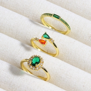 Detailed view of three gold rings with emerald and zircon stones in a beige jewelry box