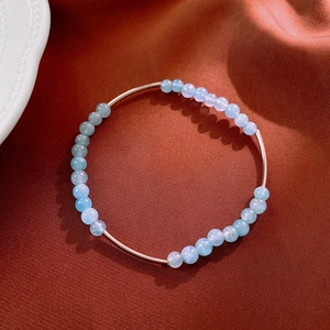 Macro detail of aquamarine beads and gold metal tube on a reddish textured fabric