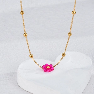 Close-up of golden beaded chain necklace featuring a magenta woven flower pendant