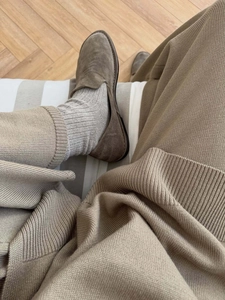Détail de mocassins en daim marron foncé portés avec un pantalon en tricot beige