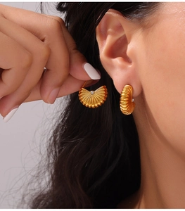 Close-up of gold fan-shaped earrings with ribbed texture and central zircon stone