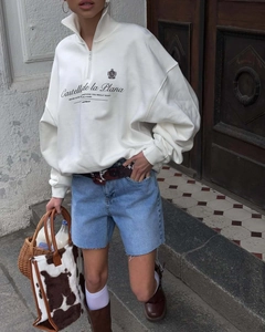 Detail of white half-zip stand collar sweatshirt with vintage graphic and blue denim shorts