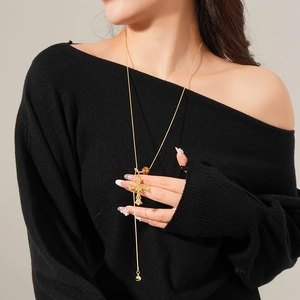 Detail of gold cross pendant necklace featuring brown tiger eye bead and small bell charm