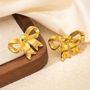 Close-up of golden metal bow earrings on a wooden tray with elegant silk fabric