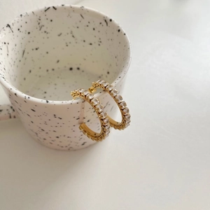 Chic gold-plated C-shaped earrings with square zircons hanging on a ceramic cup