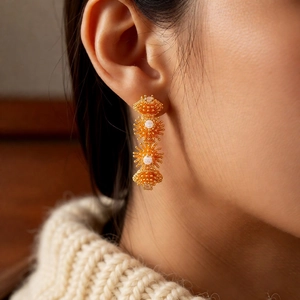 Détail de boucles d'oreilles fleuries plaquées or 18k avec perles et pompons fins