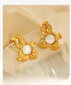 Close-up of gold flower earrings with white stones hanging on a transparent glass edge