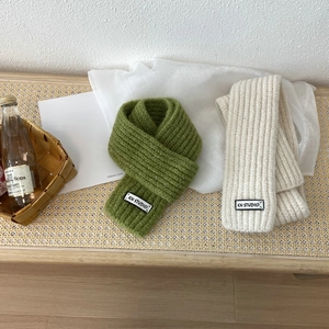 Close-up of green and beige knitted scarves showing soft wool texture and studio labels