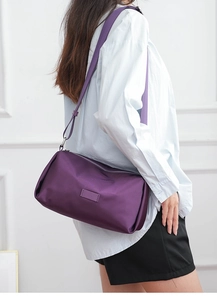 Detalle de bolso bandolera de nailon morado con correa ancha y herrajes plateados en modelo