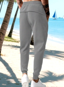 Vista posteriore dei joggers grigi da uomo con polsini elastici su sfondo di spiaggia