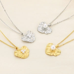 Detailed view of gold and silver leaf necklaces with elegant pearls on beige fabric