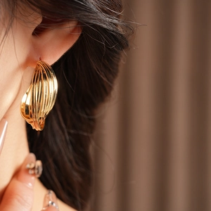 Close-up of a model wearing multi-layered gold twisted hoop earrings with a polished finish