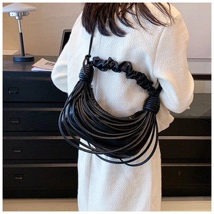 Fashionable black pleated shoulder bag with tassel fringe detail shown in street style