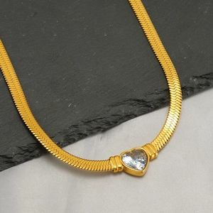 Golden heart pendant necklace with zircon and snake chain on a textured stone surface