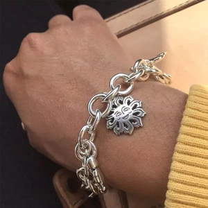 Detail shot of a silver chunky chain bracelet with a sun face pendant on a wrist.