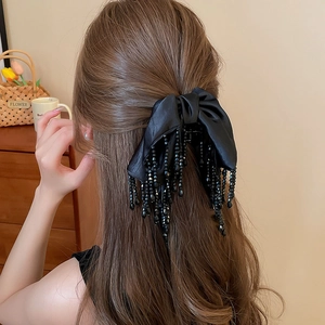 Détail d'une pince à cheveux avec nœud en soie noire et franges perlées sur un mannequin