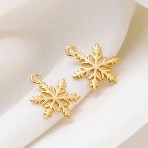 Close-up of two minimalist 18K gold snowflake charms on white silk for DIY jewelry