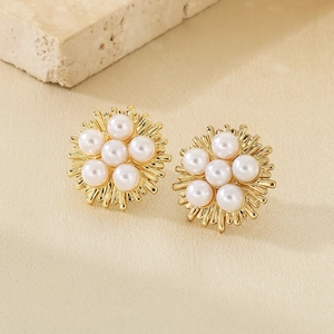 Detailed close-up of gold sunflower earrings featuring white pearls on natural stone