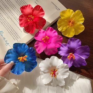 Vibrant six-color hibiscus flower hair clips on a wooden surface with a magazine backdrop