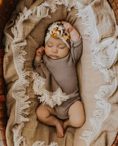Detail of infant in brown ribbed bodysuit with floral turban on a fringed blanket