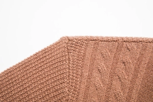 Close-up of brown knit cardigan showing detailed cable stitch texture and shoulder seam