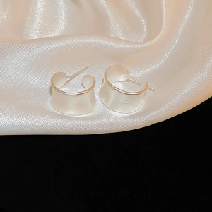Detail view of silver matte finish C-shaped earrings on elegant white satin background