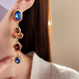 Close-up of vintage gold tassel earrings with blue and deep red gemstones on model