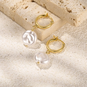 Detail of baroque pearl charms on golden hoop earrings set against a natural stone