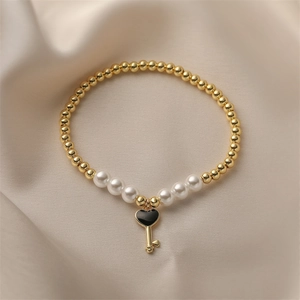 Golden bead and pearl bracelet featuring a black heart-shaped key pendant on silk