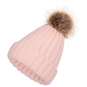 Detail of pink ribbed knit beanie featuring a large fluffy brown faux fur pompom top