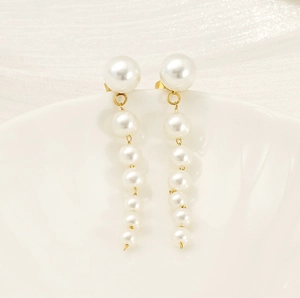 Detail of drop earrings with white pearls in decreasing sizes on gold-plated stainless steel