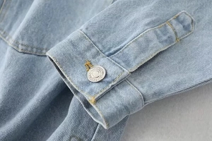 Close-up of light blue denim shirt cuff with metal button and precision stitching detail