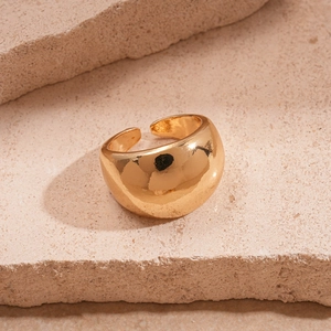 Artistic close-up of a wide gold minimalist open ring on beige textured stone background