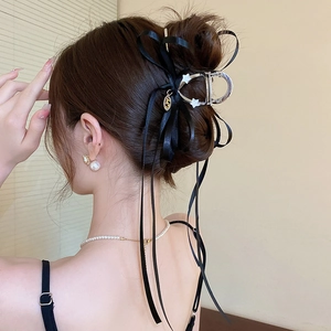 Détail d'une pince à cheveux avec nœud en ruban noir et pendentif doré sur le mannequin
