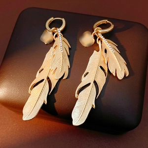 Detailed close-up of gold feather earrings with sparkling white inlaid diamonds