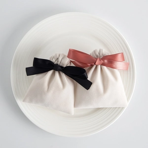Detail of cream plush jewelry pouch featuring elegant black and pink satin ribbon bows