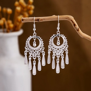 Ethnic silver-style earrings with hollow patterns and tassel pendants on a wooden branch