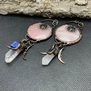 Detail of vintage sun face pendant with rose quartz and raw crystal on rustic wood bark