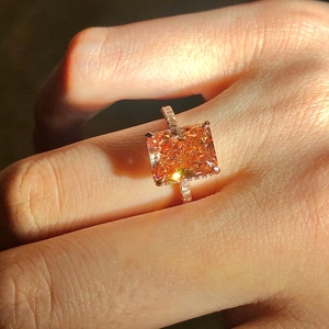 Macro view of orange radiant cut diamond ring with rose gold band on finger