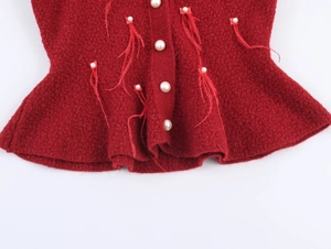 Detail of red knit cardigan featuring white pearl buttons and decorative feather fringe