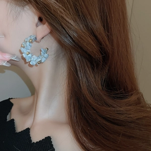 Detail of a C-shaped earring with light blue stones and gold beads on a model