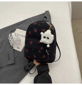 Detail of strawberry corduroy backpack with a cute white plush monster keychain charm